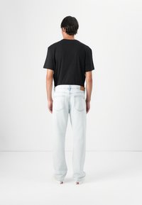 T-shirt en coton noir associée à un jean en denim bleu clair. Le jean a une coupe droite et des poches arrière avec une pièce en cuir.