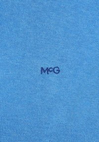 Blue knitted fabric with a smooth texture. Features a small navy "MFG" logo. Even color distribution across the material.