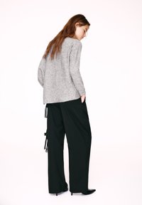 Maglione grigio in maglia dalla vestibilità comoda, abbinato a pantaloni larghi neri con nappine laterali e tasche posteriori. Scarpe nere con tacco completano il look.