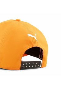 Pomarańczowa czapka z białym logo Pumy; ma teksturowany czarny regulowany pasek z otworami wentylacyjnymi. Gładka powierzchnia materiału.