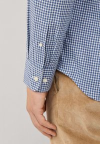 Camisa a cuadros azul y blanca con puños abotonados. La tela parece texturizada, combinada con pantalones de pana color beige.