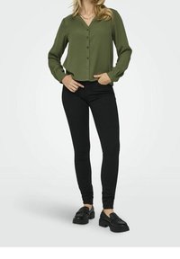 Olive green button-up shirt with long sleeves, v-neck, and a straight cut, paired with black fitted pants and black loafers.