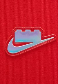 Logo Nike in materiale iridescente, caratterizzato da un design stratificato e uno sfondo rosso, con una superficie texturizzata e un distintivo accento swoosh.