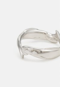 Pulsera de plata con forma de peces entrelazados, que presenta un acabado liso y pulido con un sutil detalle en los peces y un diseño abierto.