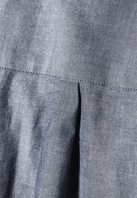 Blauer struktierter Stoff mit leichtem Glanz, der eine horizontale Naht und eine Faltenoptik am unteren Rand aufweist.