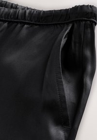 Section de pantalon noir à cordon montrant une taille élastique et une poche latérale avec couture visible.