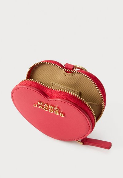 Μικρό κόκκινο πορτοφολάκι για κέρματα σε σχήμα καρδιάς με χρυστό φερμουάρ και λογότυπο Marc Jacobs, ανοιχτό για να δείχνει εσωτερικό από μπεζ ύφασμα και κρικάκι για κλειδιά.