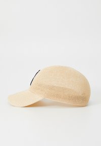 Vevd stråhatt i beige med buet skygge og svart aksent på siden; lett materiale med strukturert overflate.