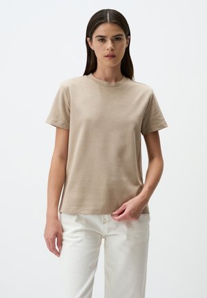Maglietta beige a maniche corte in tessuto morbido e liscio con scollatura a girocollo, vestibilità dritta e dettagli di cucitura minimal, abbinata a jeans bianchi.