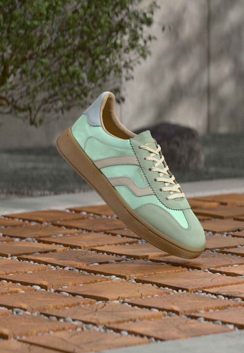 Baskets vert clair en daim texturé avec des accents en cuir lisse. Comprend des lacets crème, une semelle beige et deux bandes horizontales.