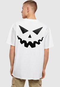 Hvid bomulds t-shirt med et stort sort græskaransigt på ryggen, med spidse øjne og en takket mund.