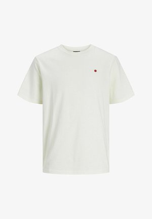 Kreklveida piedurkņu krekliņš gaiši bēšā kokvilnā ar mazu sarkanu punktiņu akcentu kreisajā krūtī. Gluda tekstūra, ikdienišķs dizains.