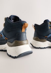Marineblå høje sneakers med tekstureret strikket overdel, orange accenter og en chunky hvid sål med et gråt prikket panel.
