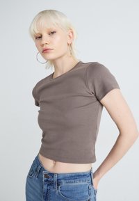 Tricou scurt, de culoare maro, confecționat dintr-un material moale, având mâneci scurte și o formă ajustată. Purtați cu blugi de culoare albastru deschis, cu talie înaltă.