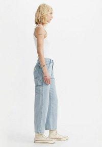 Jeans in denim di un azzurro chiaro con vestibilità relaxed, dotati di ampie tasche laterali e dettagli di cucitura. Abbinati a sneakers alte beige.