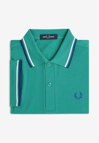 Polo vert Fred Perry avec col et manches rayés bleu et blanc, plié avec logo de la marque visible sur la poitrine.