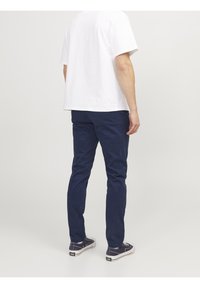 Navy blue cotton chinos with a slim fit. Features front pockets, back pockets, and a smooth texture. Worn with a plain white t-shirt and sneakers.