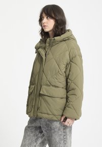 Chaqueta de plumas verde oliva con un diseño acolchado, bolsillos frontales y una capucha con cremallera y cierre a presión.