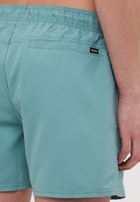 Svetle modré plavky na elastický pás, s kapsou na zadní straně a malou značkovou visačkou. Hladký povrch s minimálními detaily šití.