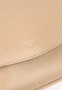 Sac en cuir beige texturé avec un rabat courbé et un logo blanc "CELINE PARIS" embossé au centre avant.