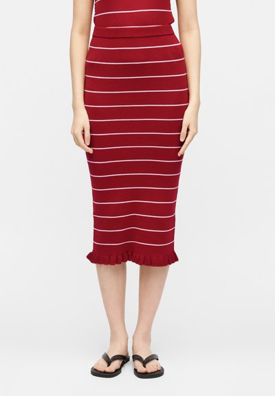 Γυναίκα που φοράει κόκκινη εφαρμοστή μίντι φούστα με λεπτές λευκές οριζόντιες ρίγες και βολάν στο τελείωμα, σε συνδυασμό με μαύρα σαγιονάρες.
