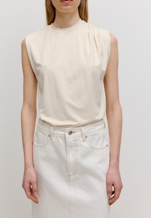 Crème mouwloos topje met een hoge halslijn, voorzien van subtiele draping bij de schouder; gecombineerd met een lichte denimrok met contrasterende stikken.