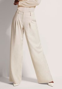 Brede broek in lichtbeige stof met een subtiele textuur, voorzien van plooien aan de voorkant, een knoopsluiting en zijzakken.