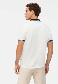 Weißes Poloshirt mit einem schwarzen Kragen und bunten gestreiften Akzenten an den Ärmeln. Kurze Ärmel, Seitenschlitze und eine glatte Textur.
