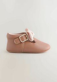 Light pink leather baby shoe with a rounded toe, scalloped cutout, and a decorative bow, featuring a side buckle for closure. Soft sole.
