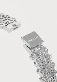Sølvarmband med blomstermønster. Har en jevn lås med innskriften "kate spade." Lett metallmateriale.