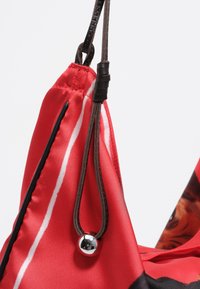 Czerwona torba z tkaniny z czarnymi akcentami, z błyszczącą srebrną kulą na sznurku, szczegółowo wykończona gładką teksturą i paskowanym wzorem.