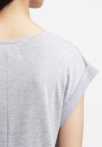 Harmaa lyhythihainen paita pyöreällä kaula-aukolla ja käännetyillä hihoilla; pehmeä, kevyt kangas, jolla on sileä rakenne. Takakuvassa näkyy saumat.