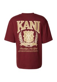 Maroona īsām piedurknēm T-kreklā ar bēša "KANI" logo, vairogā, lauru vainagā un uzrakstu "Bruklina, Ņujorka" aizmugurē.