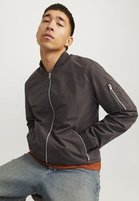 Men's bomber jacket in dark gray fabric with a zip front, ribbed collar, two side pockets, and an additional zip pocket on the sleeve.