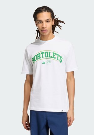 Ung mand med dreadlocks iført en hvid T-shirt med grøn "Portoleto"-tekst og logoer, kombineret med blå bukser mod en ensfarvet baggrund.