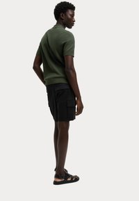 Polo shirt verde scuro a maniche corte con colletto a costine, abbinato a pantaloni cargo neri con tasche laterali e sandali piatti.