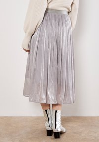 Falda midi plisada plateada con una textura suave, que presenta una cinturilla ancha y un ligero brillo, combinada con botas de tobillo plateadas y brillantes.