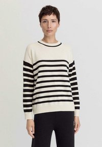 Gestreiftes Strickpullover in Creme und Schwarz mit Rundhalsausschnitt, langen Ärmeln und geripptem Saum. Das Material wirkt weich und hat einen lockeren Schnitt.