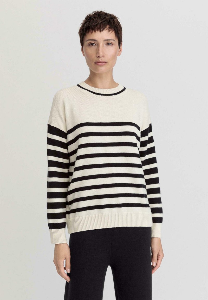 Gestreiftes Strickpullover in Creme und Schwarz mit Rundhalsausschnitt, langen Ärmeln und geripptem Saum. Das Material wirkt weich und hat einen lockeren Schnitt.