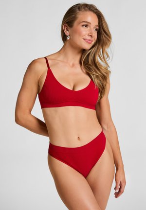 Roter gerippter Bikini-Oberteil mit dünnen Trägern und tiefem V-Ausschnitt, kombiniert mit passenden hochgeschnittenen Bikini-Hotpants. Glatte Textur überall.