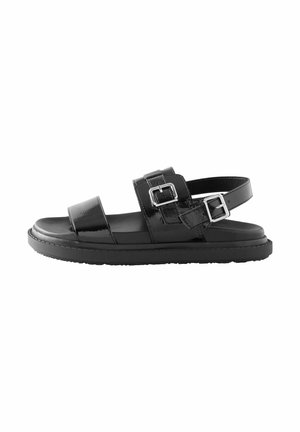 Black sandal featuring two wide straps with metallic buckles, a sleek patent finish, and a flat rubber sole.