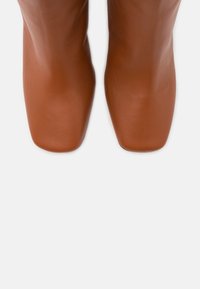 Bottes de cheville en cuir marron avec un design épuré, des orteils carrés et une texture lisse. Les semelles sont plates et légèrement arrondies.