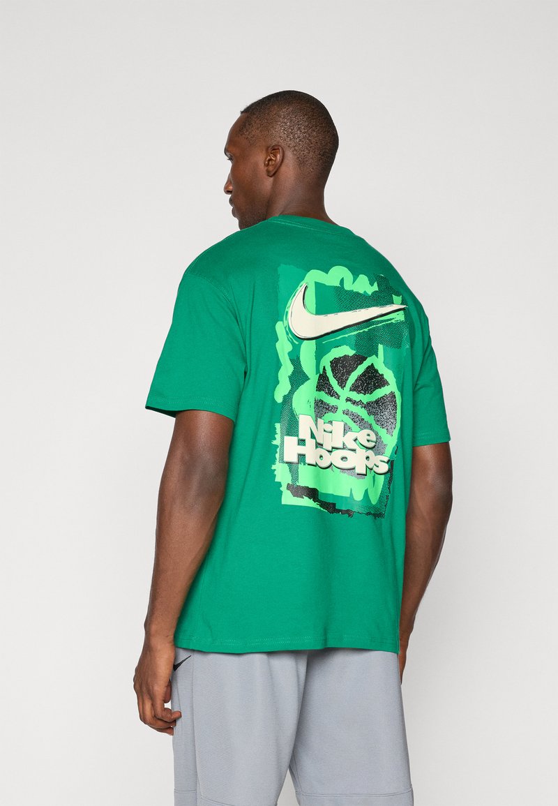 Grøn bomulds-t-shirt med et stort grafisk motiv på ryggen, der viser Nike-logoet, teksten "Nike Hoops" og et basketball-design i kontrasterende farver.