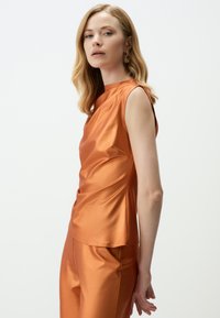 Satin oranje top met een mouwloos ontwerp, voorzien van een ronde hals en geplooide textuur, gecombineerd met bijpassende satijnen broeken.