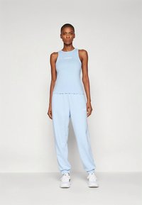 Svetlo modra športna majica brez rokavov in ujemajoče se trenirke, obe iz mehke tkanine z odtisnjenim logotipom. Joggerske hlače imajo elastične manšete in pas.