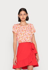 Blusa floral de mangas curtas em tons de rosa e laranja, com um decote redondo. Combinada com uma saia envolvente vermelha com bainha franzida e laço lateral.