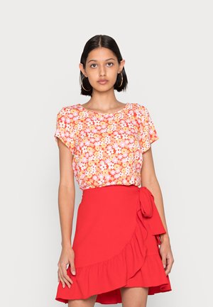 Blusa floral de mangas curtas em tons de rosa e laranja, com um decote redondo. Combinada com uma saia envolvente vermelha com bainha franzida e laço lateral.