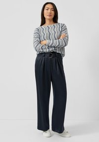 Gestreifter Pullover in Blau und Weiß mit langen Ärmeln, kombiniert mit weiten dunkelblauen Hosen; verfügt über einen Gürtel mit einer runden Schnalle.