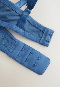 Zils josta ir ar strukturētu sietiņu un gluda auduma maisījumu, regulējamiem siksnām un āķa un cilpas aizdari drošai piegulošanai.