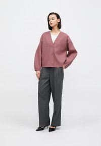 Rosa oversize tröja med V-ringning, kombinerad med högmidjade grå byxor. Svarta spetsiga skor fulländar outfiten.